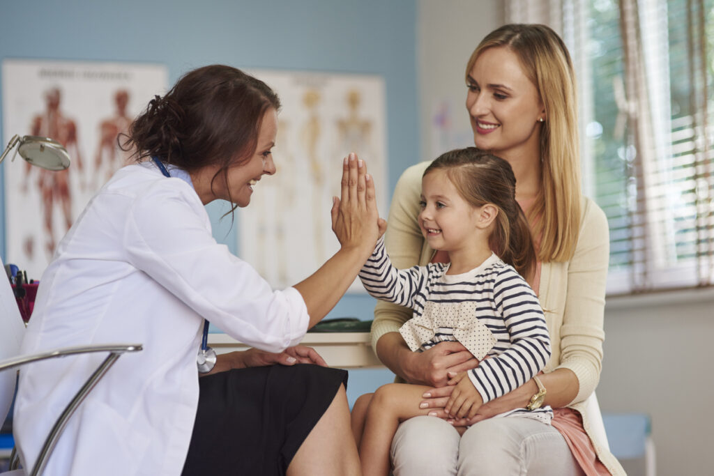Läkare gör high five med ett barn i mammans knä